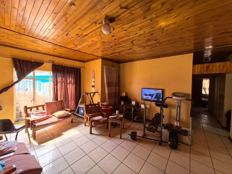 A living room featuring ceramic tiled flooring and a timber tongue and groove ceiling, providing a dated aesthetic with potential for modernization.