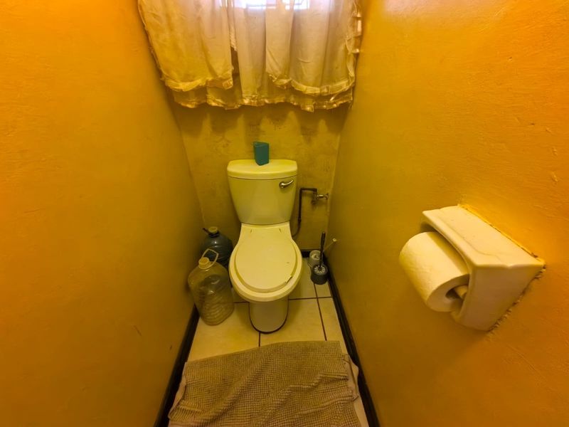 A small, dated bathroom featuring a standard toilet and tiled flooring, currently requiring cosmetic updates and wall refinishing.