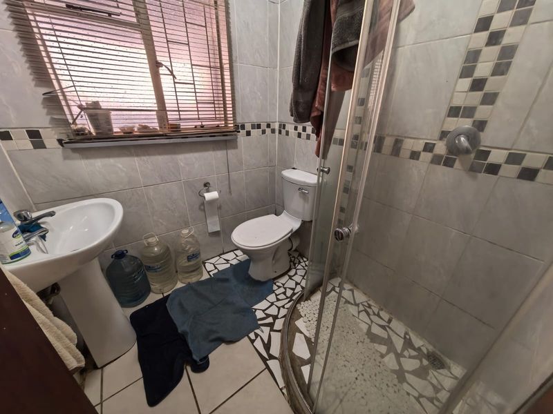 A compact bathroom featuring a pedestal basin, toilet, and a corner shower enclosure with tiled finishes.