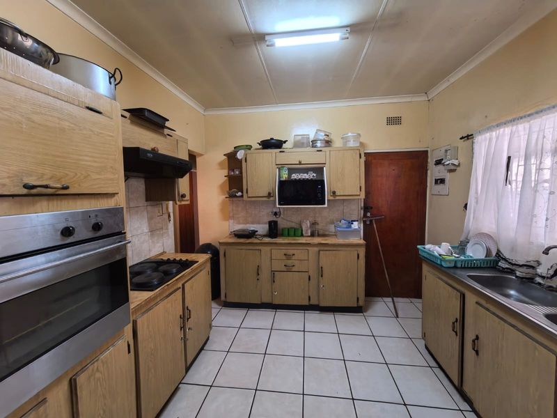 A dated kitchen featuring wood-look cabinetry, built-in oven and hob, tiled flooring, and functional layout with potential for modernization.