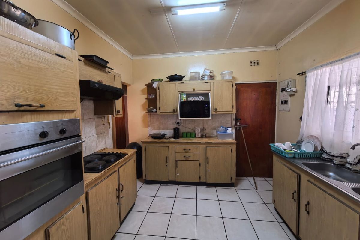 A dated kitchen featuring wood-look cabinetry, built-in oven and hob, tiled flooring, and functional layout with potential for modernization.
