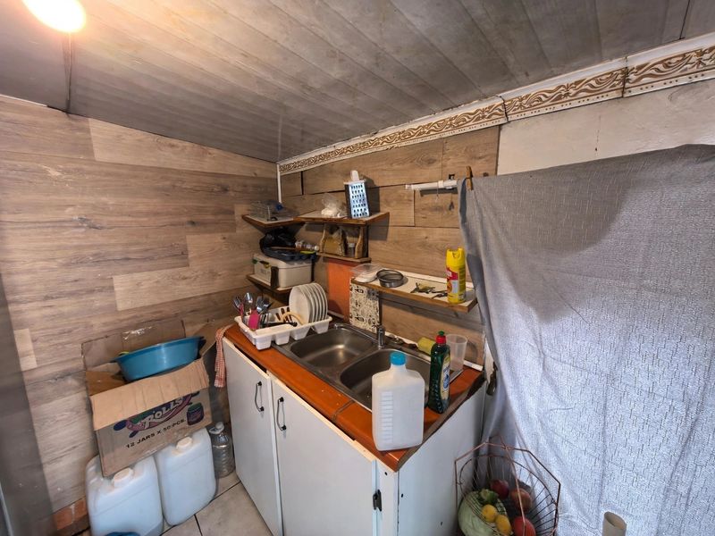 A compact scullery area featuring a double bowl sink, built-in cabinetry, and wood-look wall paneling, requiring cosmetic updates to improve functionality and aesthetic appeal.