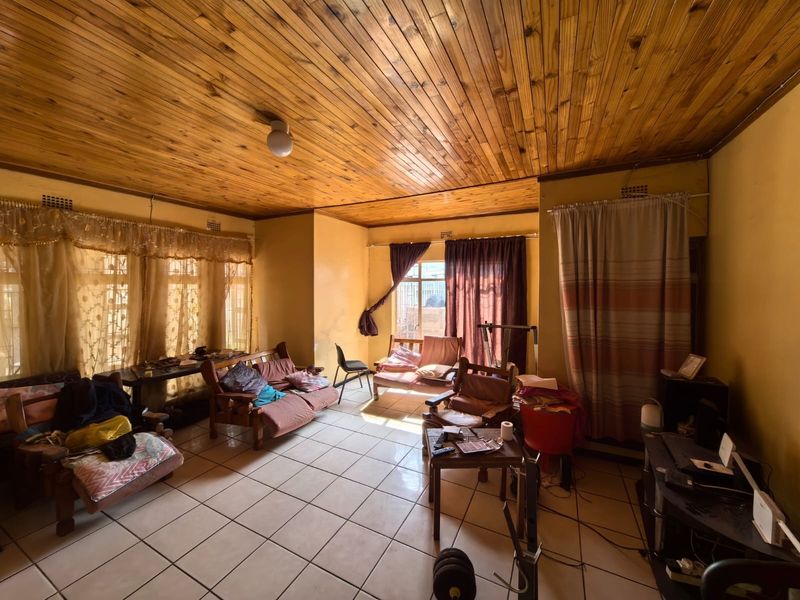 Spacious living area featuring a timber tongue and groove ceiling and ceramic floor tiles, offering a dated aesthetic with potential for modernization.