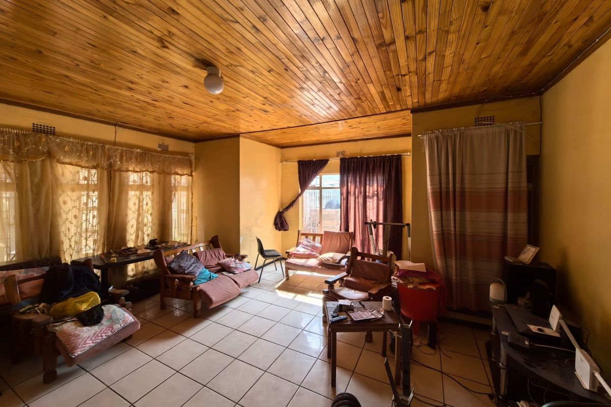 Spacious living area featuring a timber tongue and groove ceiling and ceramic floor tiles, offering a dated aesthetic with potential for modernization.