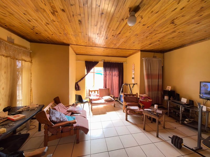 A living room featuring a timber tongue and groove ceiling and ceramic tiled flooring, offering a functional space with potential for modernization.
