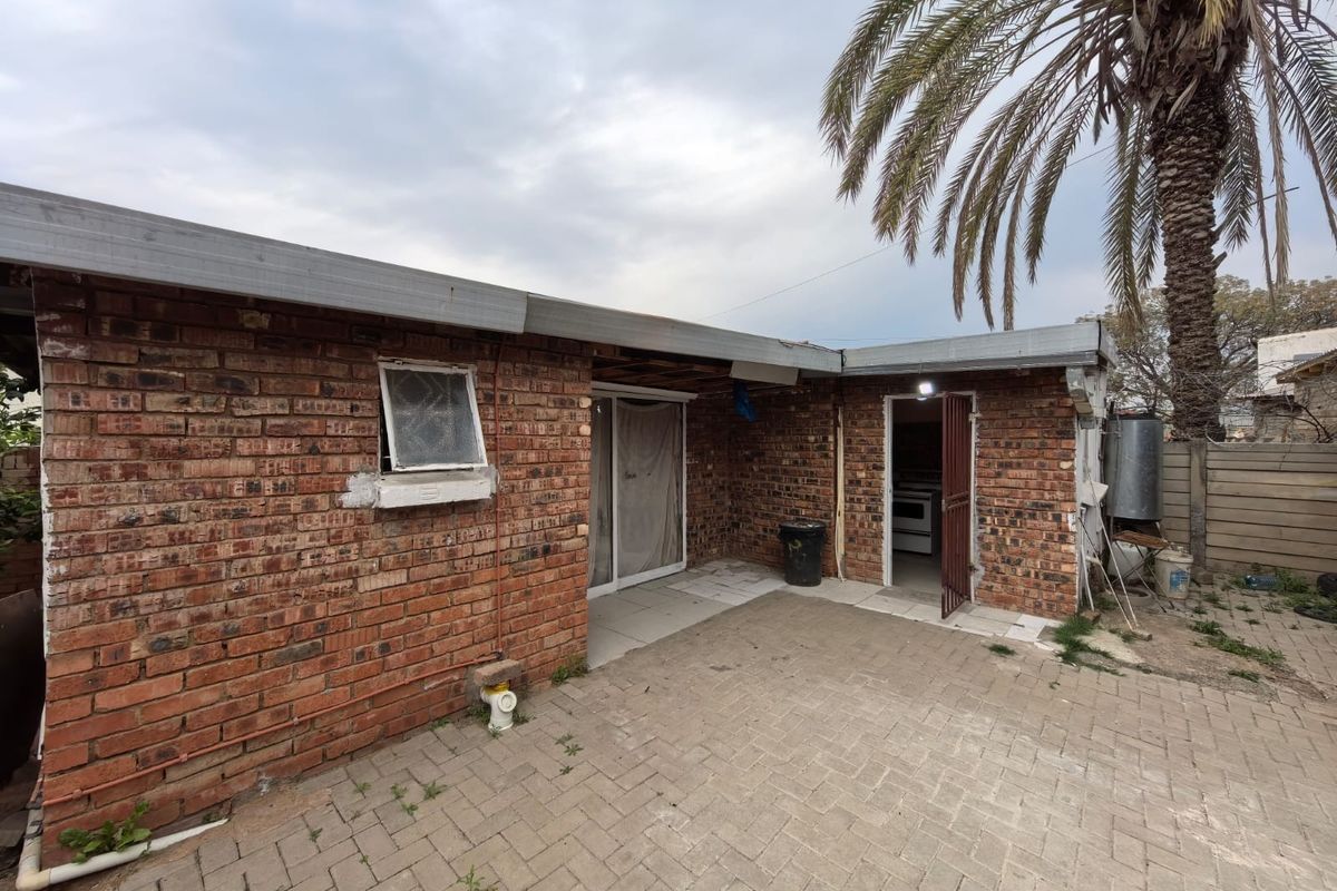 Rear exterior view of a face brick house featuring a paved patio area, sliding door access, and a security gate entrance.