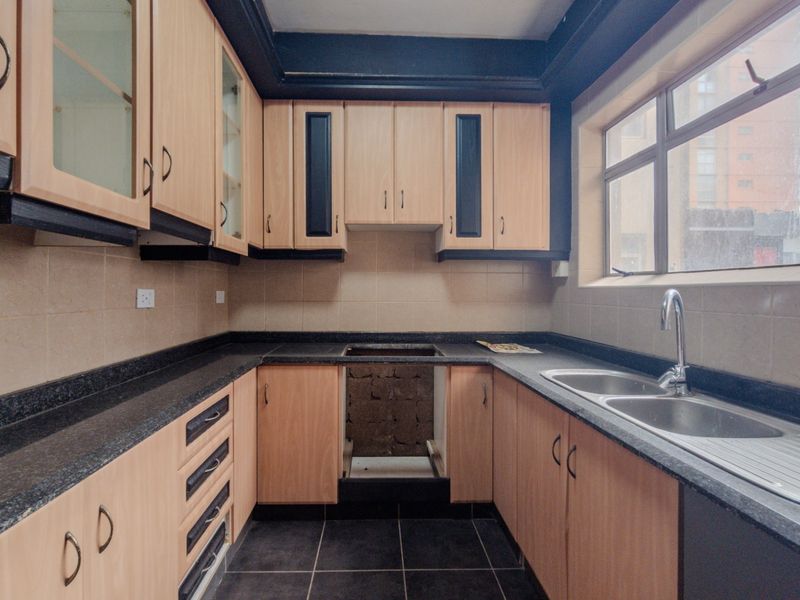 A functional kitchen featuring light wood-finish cabinetry, dark granite countertops, a double stainless steel sink, and tiled finishes, awaiting a new stove installation.