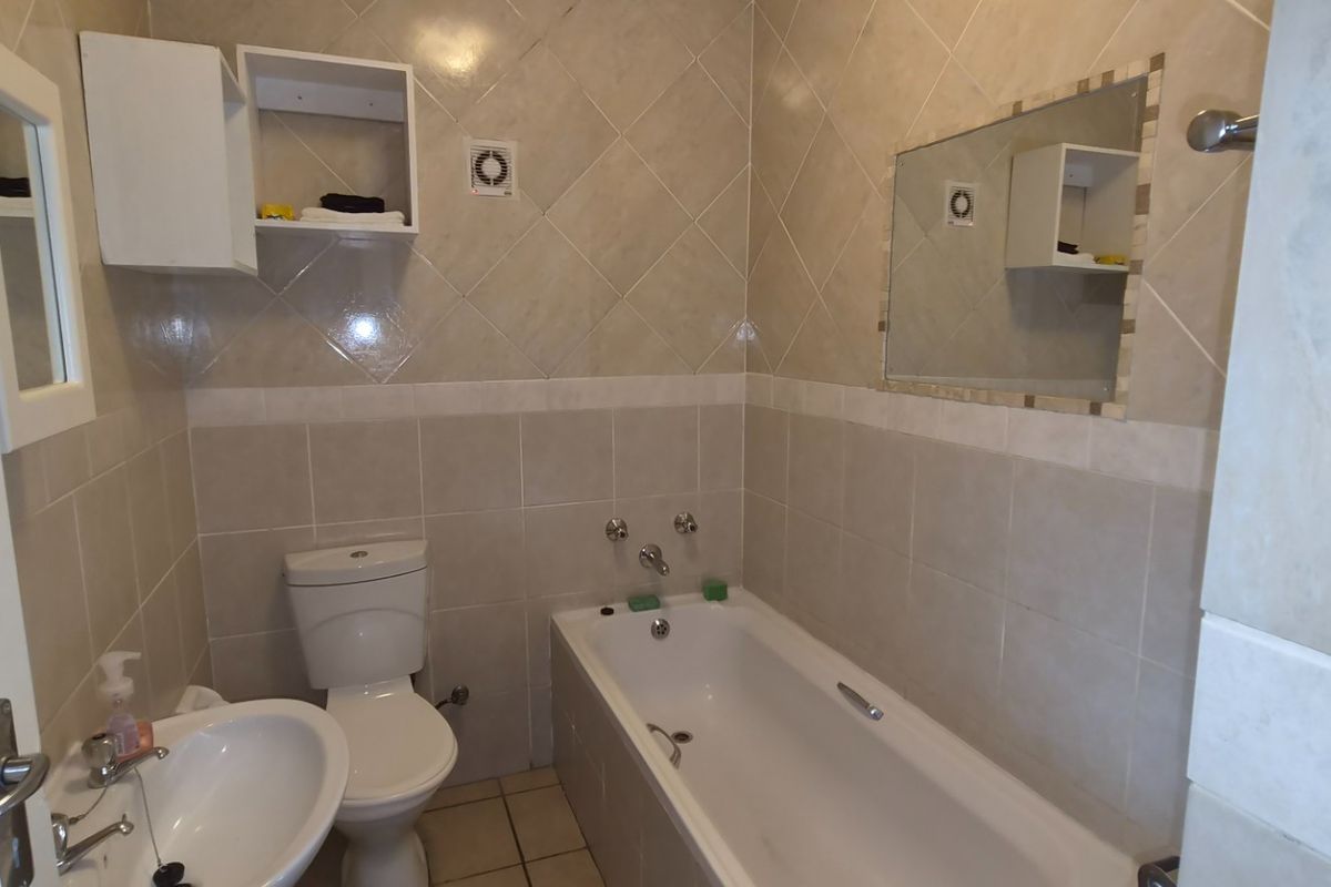 A functional bathroom featuring a bathtub, pedestal basin, toilet, and neutral wall tiling with built-in shelving and an extractor fan.