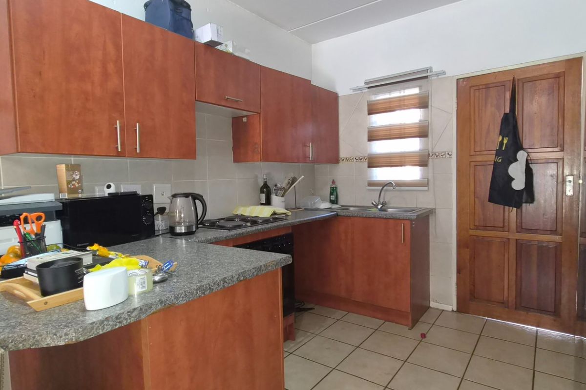 A functional kitchen featuring wood-finish cabinetry, granite-look countertops, a built-in hob, and tiled flooring, offering a practical layout for daily meal preparation.