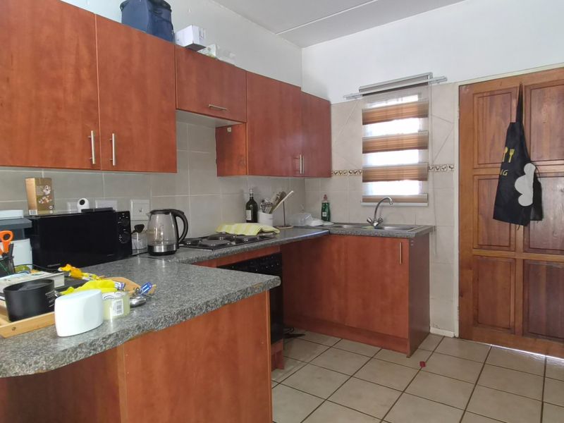 A functional kitchen featuring wood-finish cabinetry, granite-look countertops, a built-in hob, and tiled flooring, offering a practical layout for daily meal preparation.