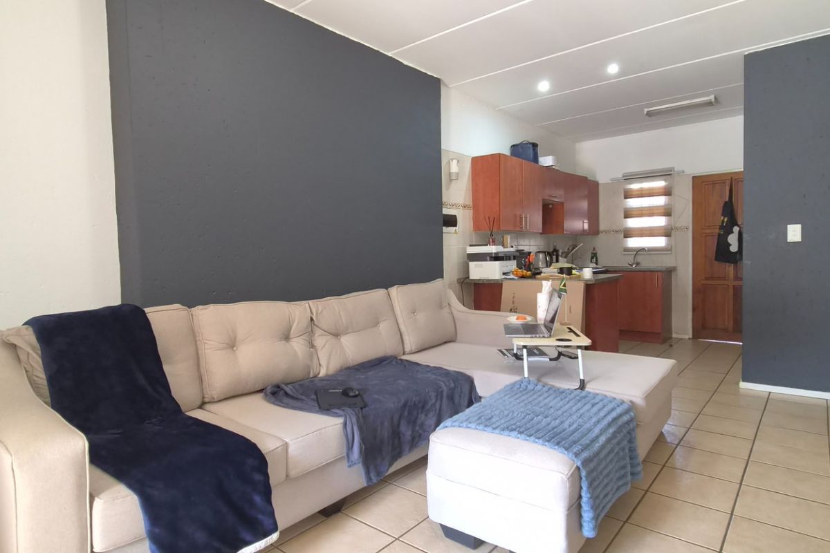 Open-plan living area featuring tiled flooring, recessed lighting, and a functional kitchen with wooden cabinetry and a sink.