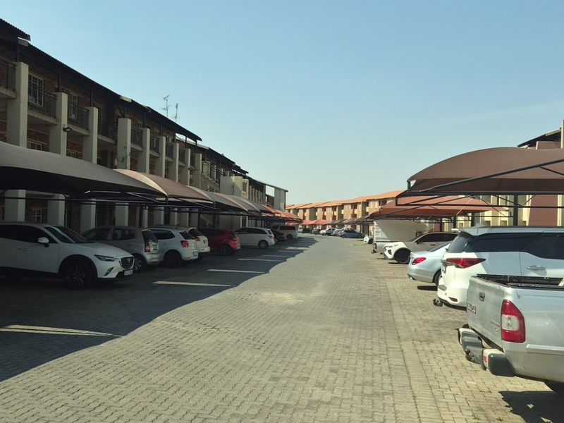 Exterior view of an apartment complex featuring a paved driveway with designated shade cloth carports for residents.