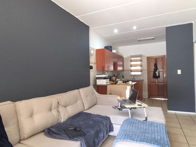 Open-plan living area featuring tiled flooring, recessed lighting, and a functional kitchen space with wooden cabinetry.
