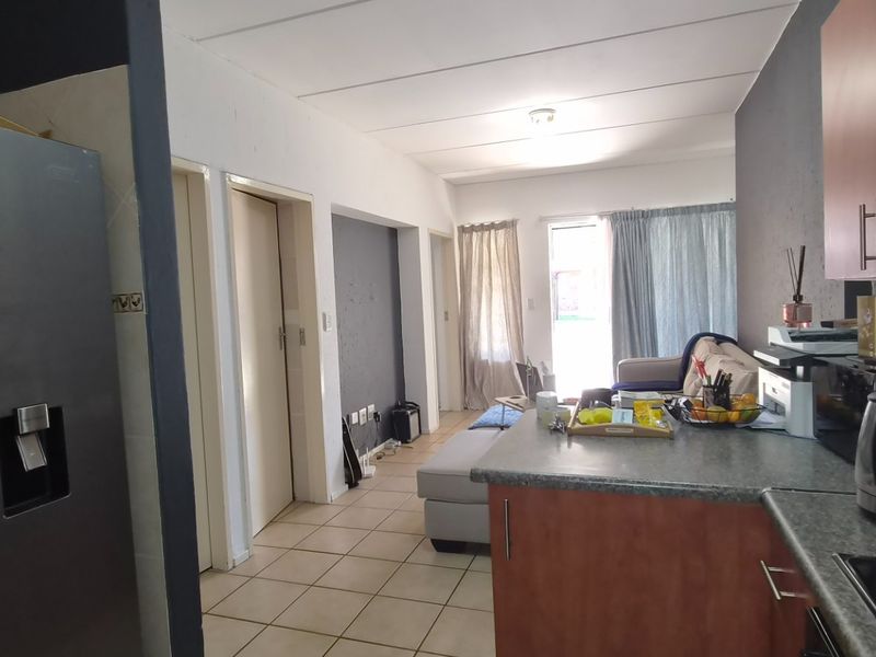 Open-plan living area featuring a functional kitchen with laminate countertops and tiled flooring, flowing into a connected living space with access to a balcony.