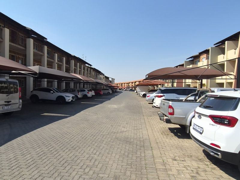 Exterior view of an apartment complex featuring a paved driveway with covered parking bays and multi-story residential units.