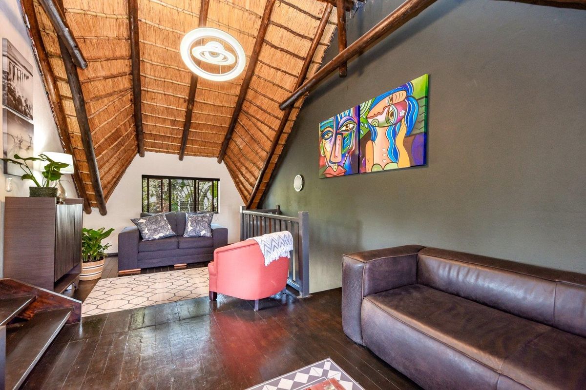 A cozy living area featuring a high vaulted thatch ceiling with exposed timber rafters and dark wood flooring, creating a warm and rustic atmosphere.