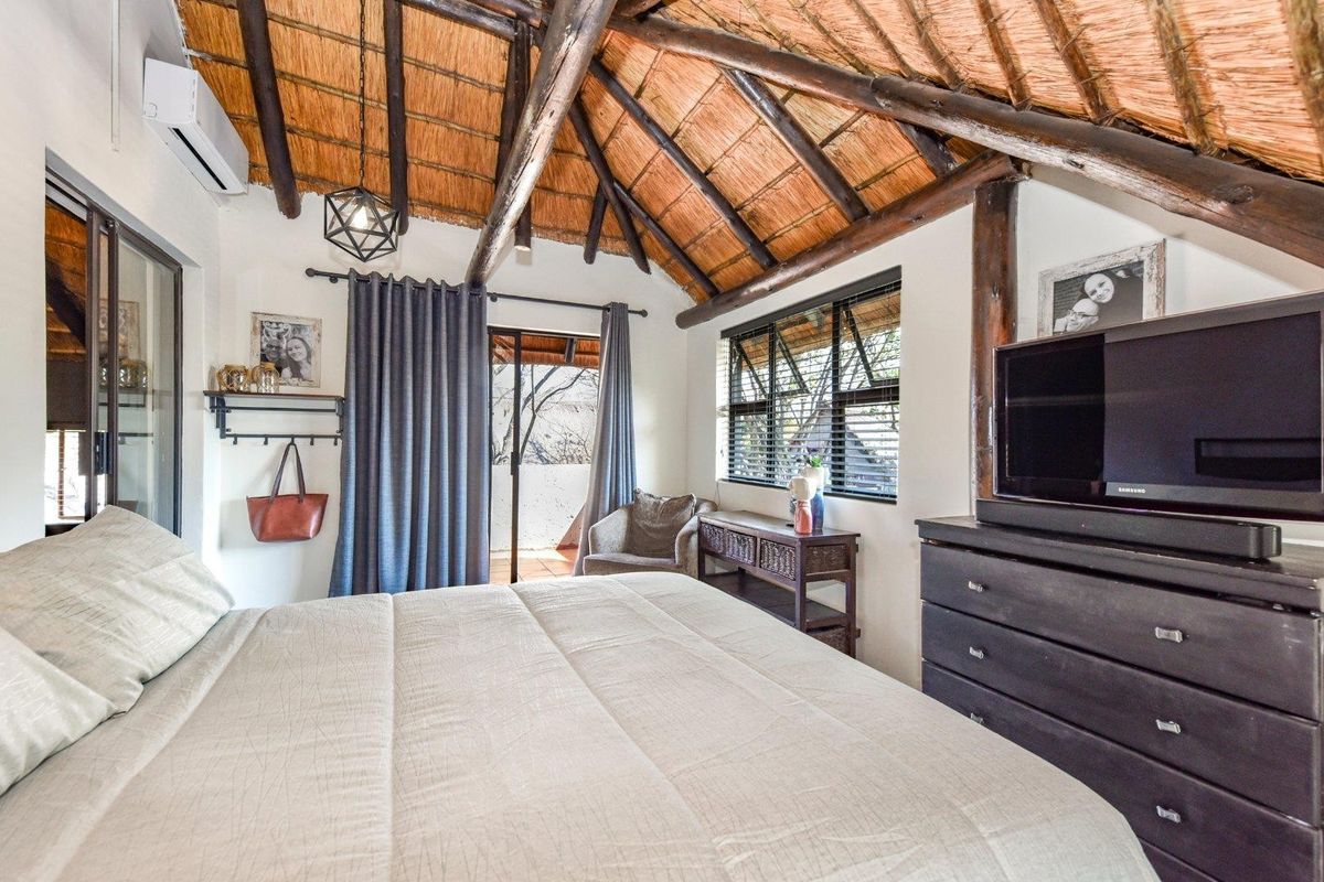 A cozy bedroom featuring a high vaulted thatched roof with exposed timber rafters, air conditioning, and direct access to a private balcony.