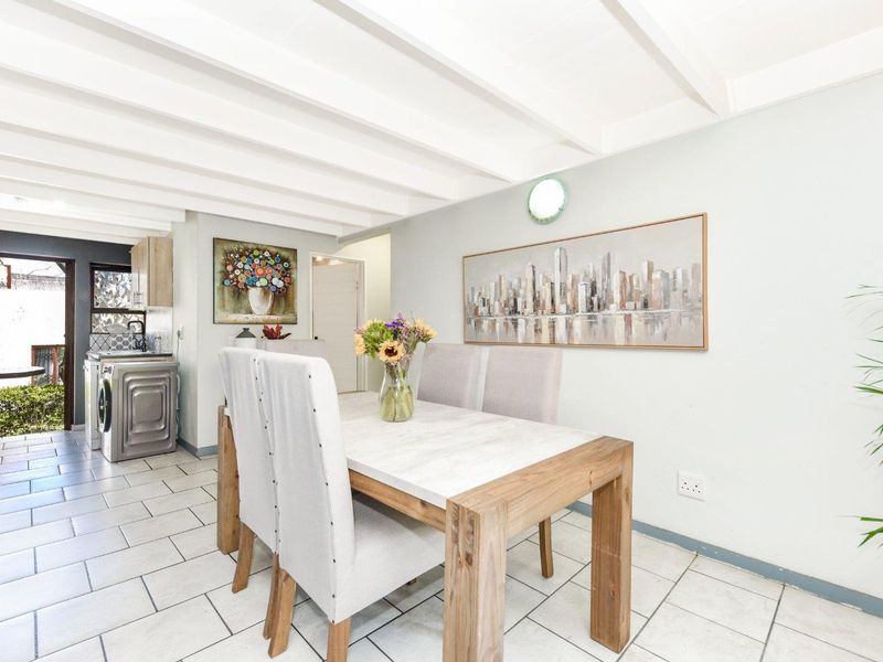 Open-plan dining area featuring exposed beam ceilings and tiled flooring, seamlessly flowing into a functional kitchen and laundry space.