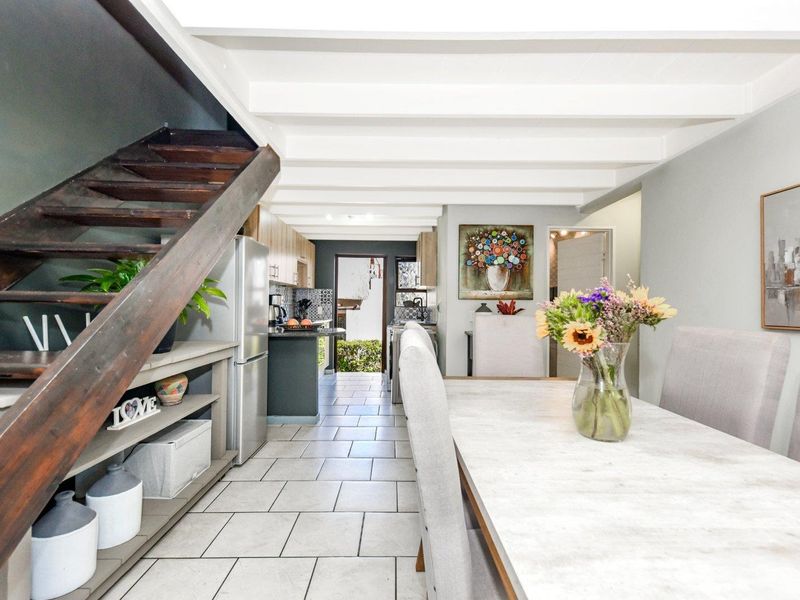 Open-plan living and dining area featuring exposed timber ceiling beams, tiled flooring, and a wooden staircase leading to the upper level.