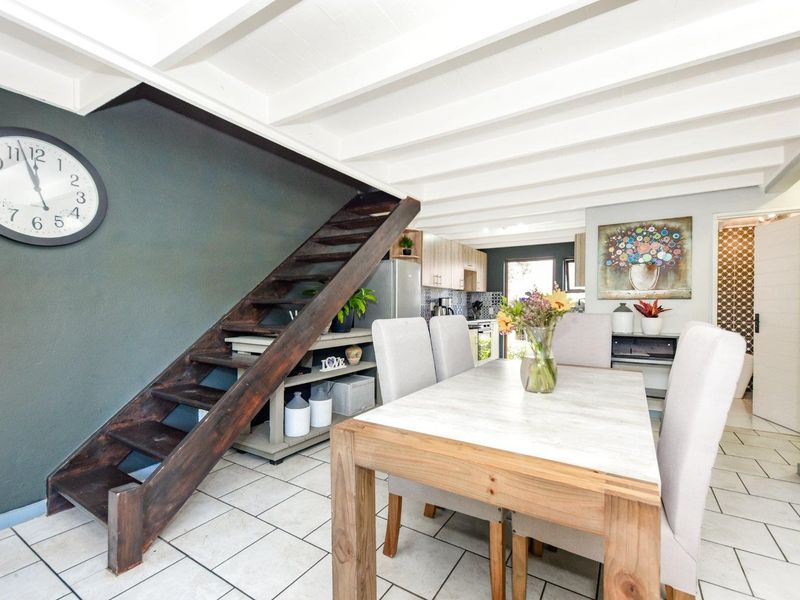 Open-plan dining area featuring exposed white ceiling beams, tiled flooring, and a wooden staircase leading to the upper level, adjacent to the kitchen.
