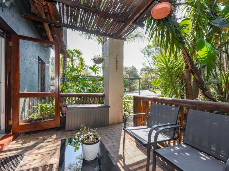 A covered patio area featuring a rustic thatched roof, timber support posts, and paved flooring, providing a shaded outdoor space for relaxation.