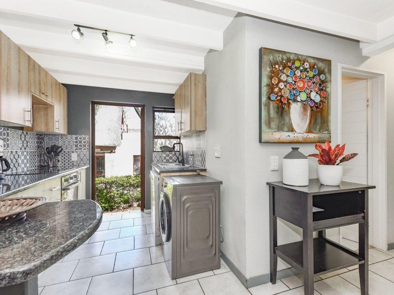 Modern kitchen featuring light wood cabinetry, stone countertops, tiled backsplash, and direct access to the exterior, complemented by exposed ceiling beams.