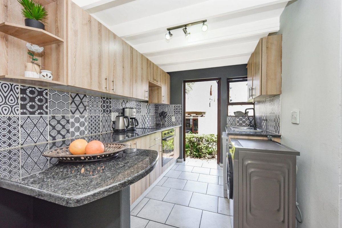 Modern galley-style kitchen featuring light wood cabinetry, granite countertops, striking patterned tile backsplash, and direct access to the exterior.