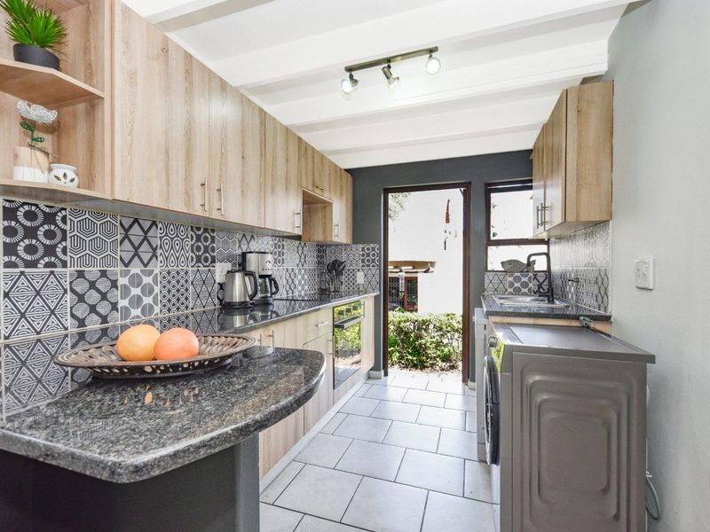 Modern galley-style kitchen featuring light wood cabinetry, granite countertops, striking patterned tile backsplash, and direct access to the exterior.