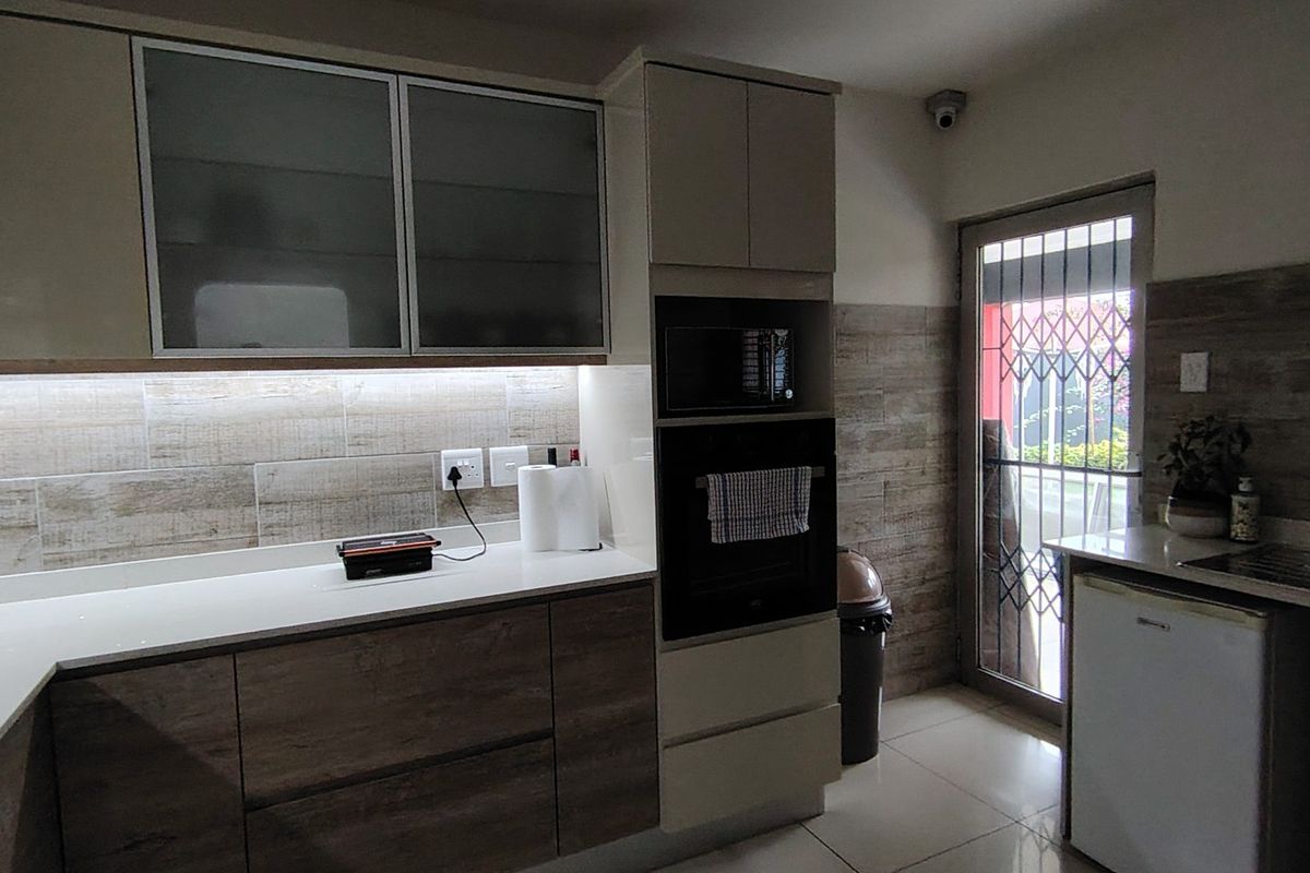Modern kitchen featuring wood-grain cabinetry, built-in oven and microwave, stone-look tiled backsplash, and direct access to the exterior via a secure glass door.