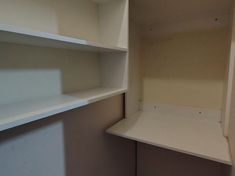 A small utility or storage alcove featuring built-in white shelving and a fixed desk surface, requiring minor cosmetic updates.