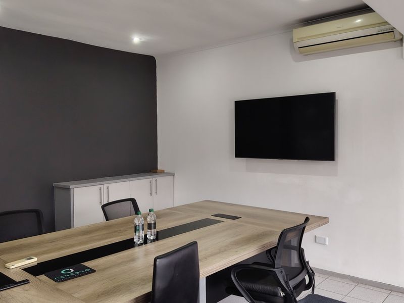 A functional office meeting room featuring a large conference table, wall-mounted television, built-in storage cabinetry, and air conditioning.