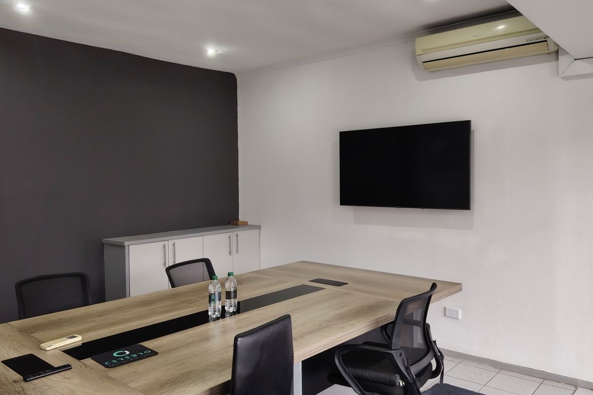 A functional office meeting room featuring a large conference table, wall-mounted television, built-in storage cabinetry, and air conditioning.
