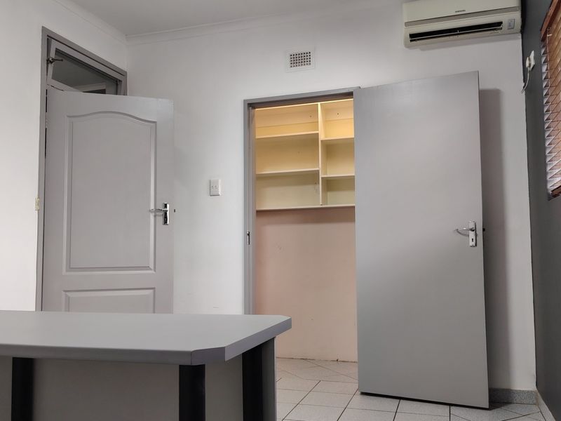 A clean, functional office space featuring tiled flooring, a wall-mounted air conditioning unit, and a separate storage area with built-in shelving.