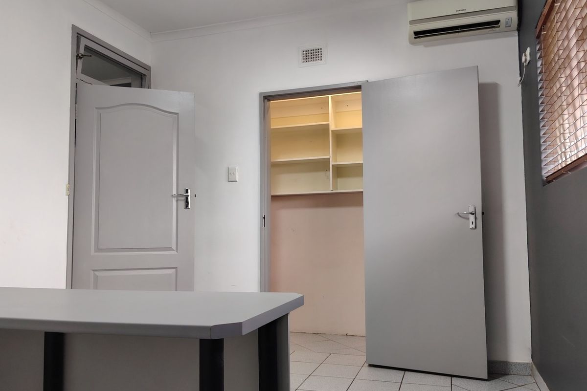A clean, functional office space featuring tiled flooring, a wall-mounted air conditioning unit, and a separate storage area with built-in shelving.