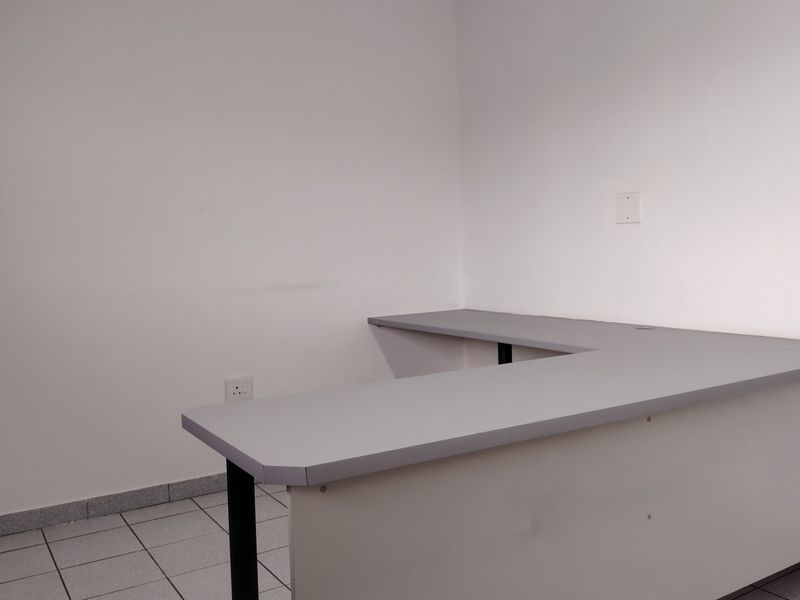 A functional office space featuring a built-in L-shaped desk, tiled flooring, and neutral wall finishes, suitable for a professional workspace.