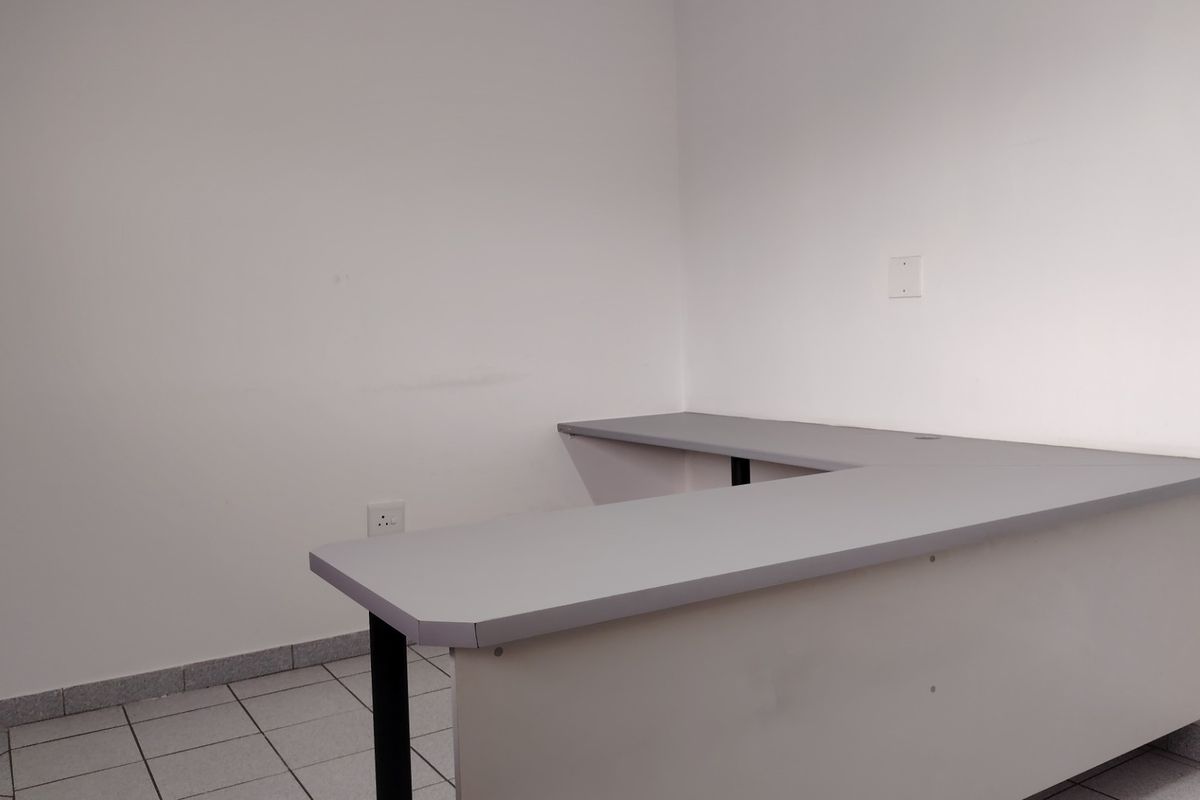 A functional office space featuring a built-in L-shaped desk, tiled flooring, and neutral wall finishes, suitable for a professional workspace.