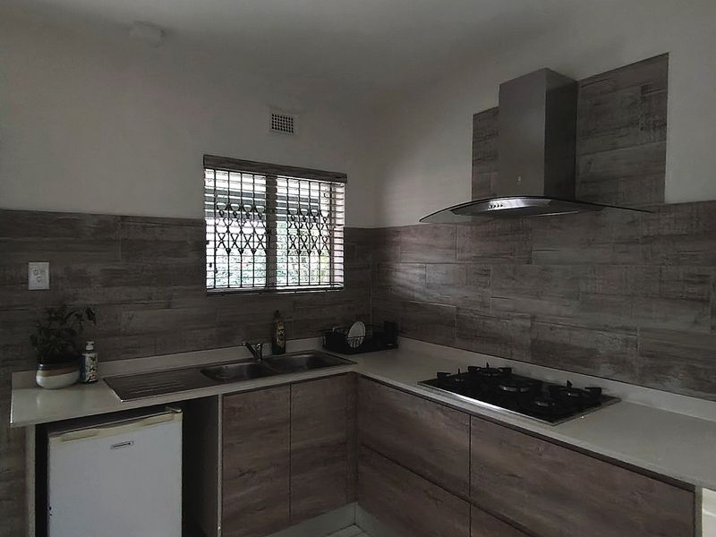 Modern kitchen featuring wood-look cabinetry, tiled backsplash, gas hob with extractor fan, and stainless steel sink, with direct access to the exterior.