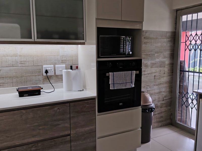 Modern kitchen featuring built-in oven and microwave, stone countertops, under-cabinet lighting, and a secure glass door leading to the exterior.