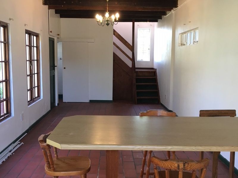 Spacious living area featuring exposed timber ceiling beams, terracotta tiled flooring, and a wooden staircase leading to the upper level.