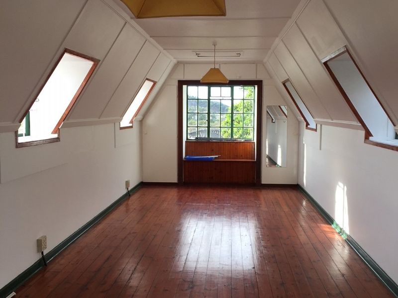 An empty attic-style bedroom featuring polished timber flooring, sloped ceilings with dormer windows, and a built-in window seat with views.