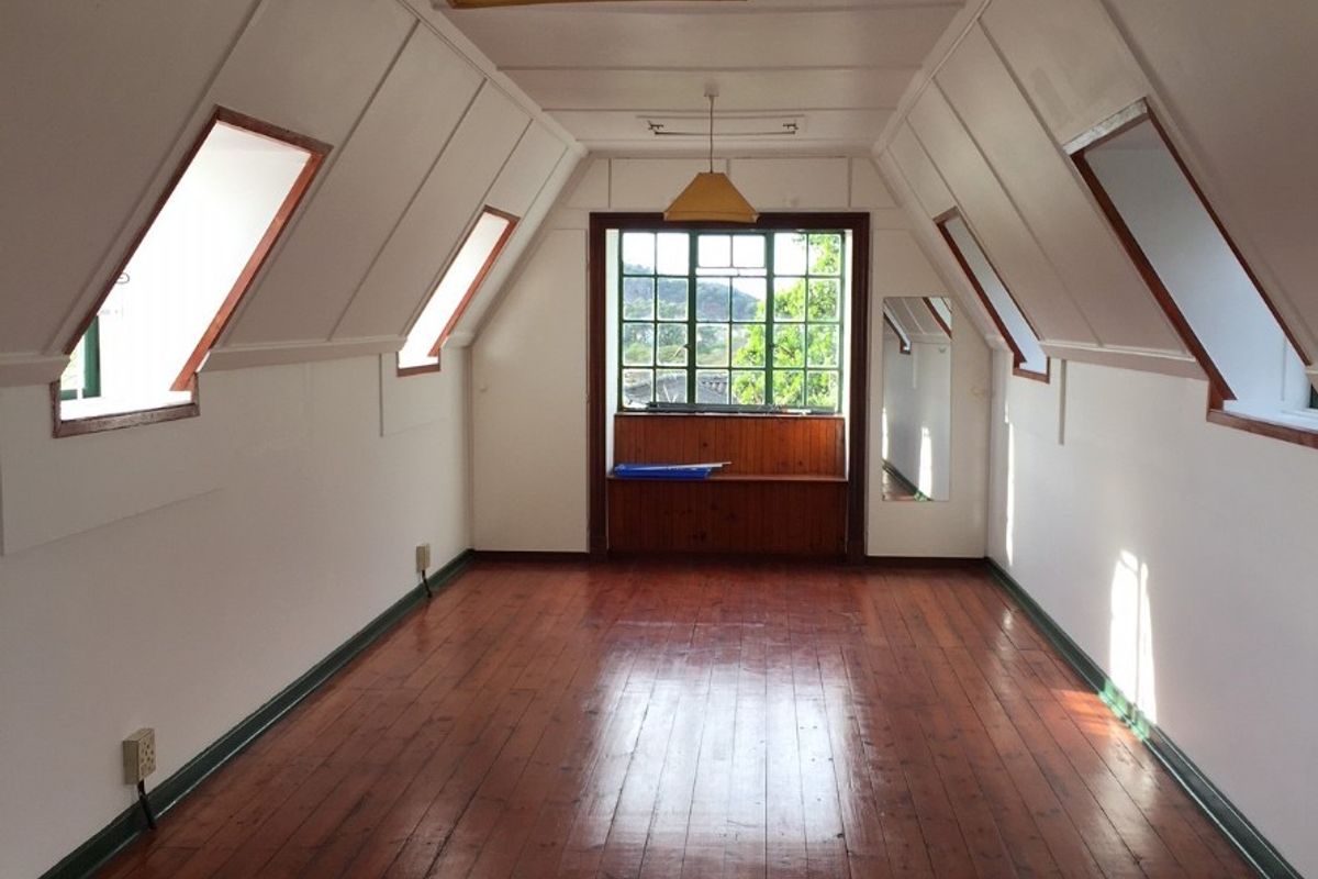 An empty attic-style bedroom featuring polished timber flooring, sloped ceilings with dormer windows, and a built-in window seat with views.