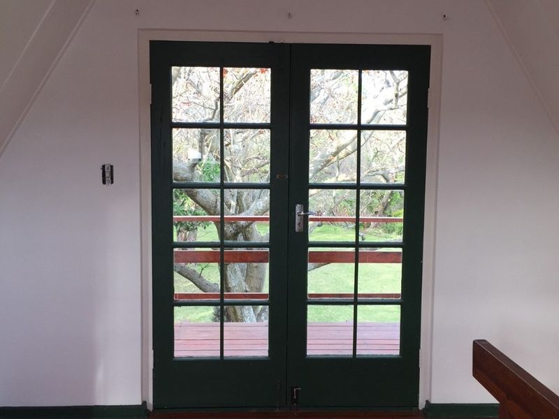 An empty bedroom featuring polished timber flooring, a vaulted ceiling, and dark-framed French doors opening onto an outdoor balcony area.