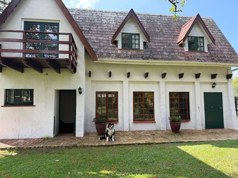 Rear elevation of a cottage featuring a timber balcony, dormer windows, and a brick patio overlooking the garden.