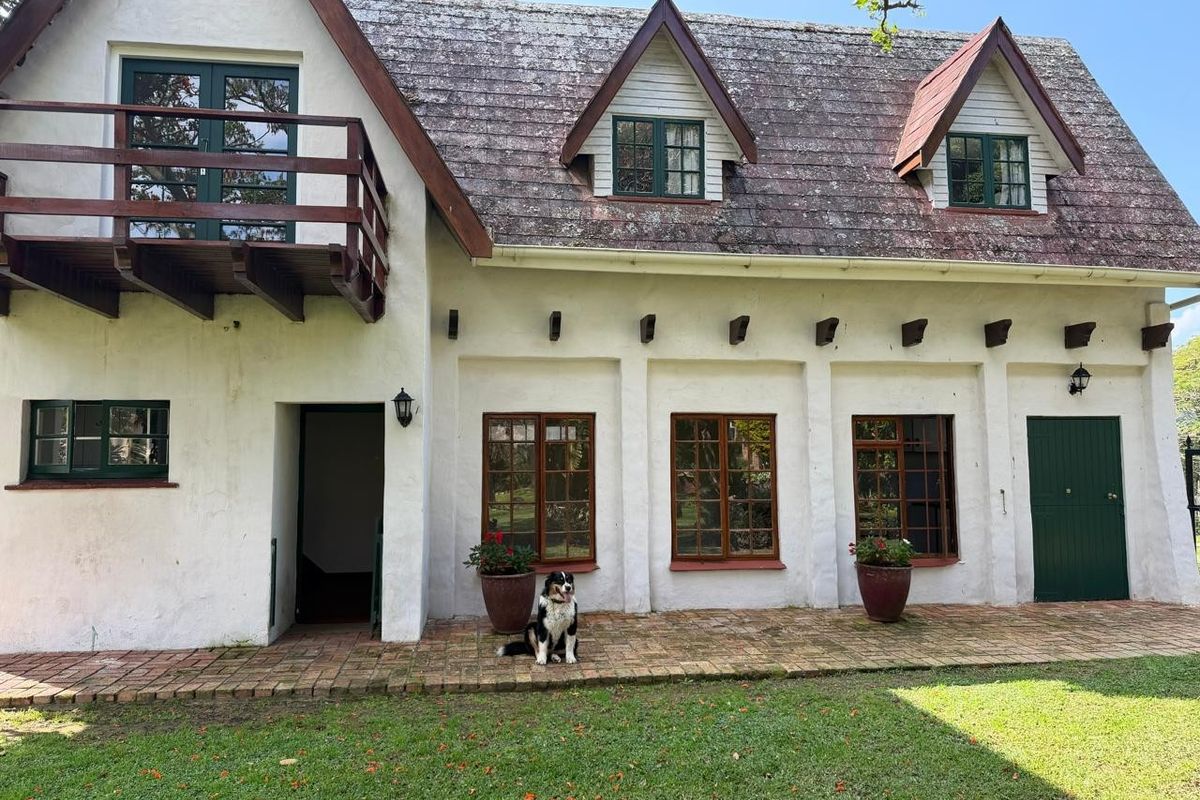 Rear elevation of a cottage featuring a timber balcony, dormer windows, and a brick patio overlooking the garden.