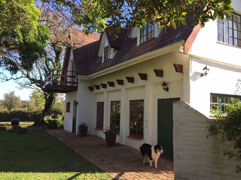 Rear view of a cottage featuring a brick patio, timber balcony, and traditional roofline with dormer windows set in a garden.