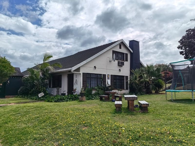 A view of the rear elevation of the house featuring a tiled roof, chimney, and established garden area.
