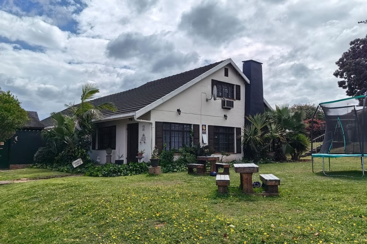 A view of the rear elevation of the house featuring a tiled roof, chimney, and established garden area.