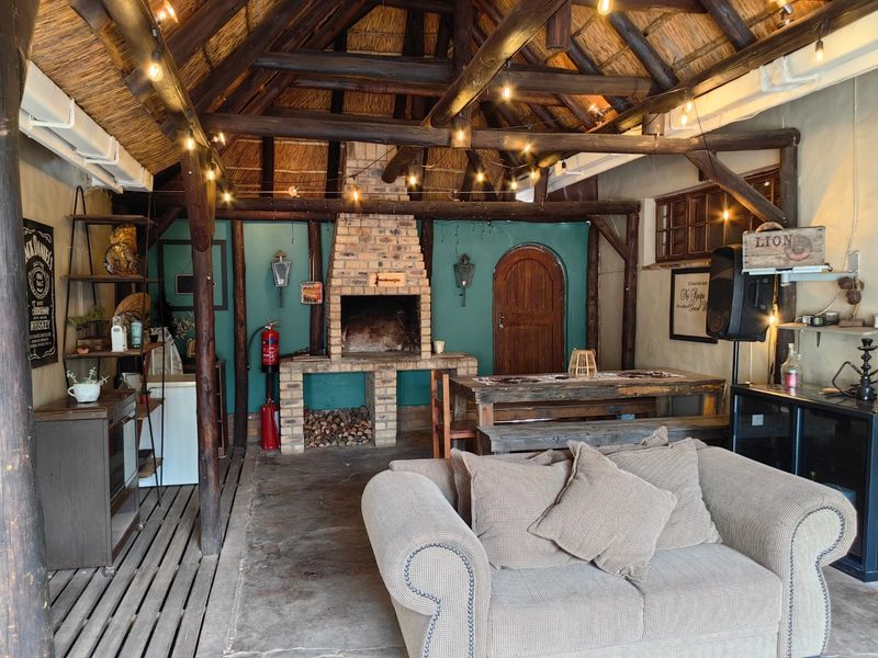 A rustic covered patio area featuring a traditional thatched roof, exposed timber beams, and a large built-in brick fireplace for outdoor entertaining.