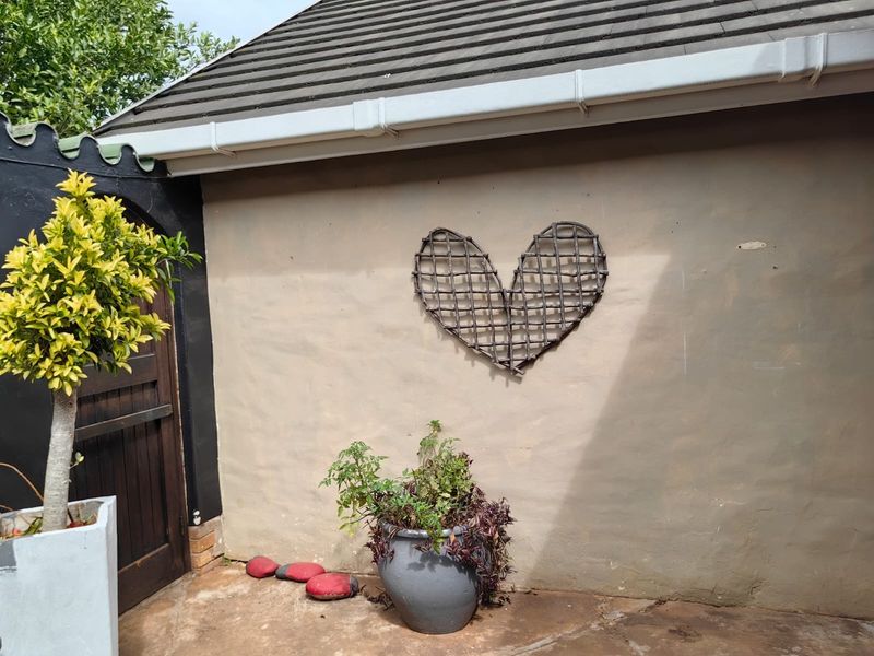 A view of a rear exterior wall featuring a tiled roof, guttering, and a wooden door leading to a paved patio area.