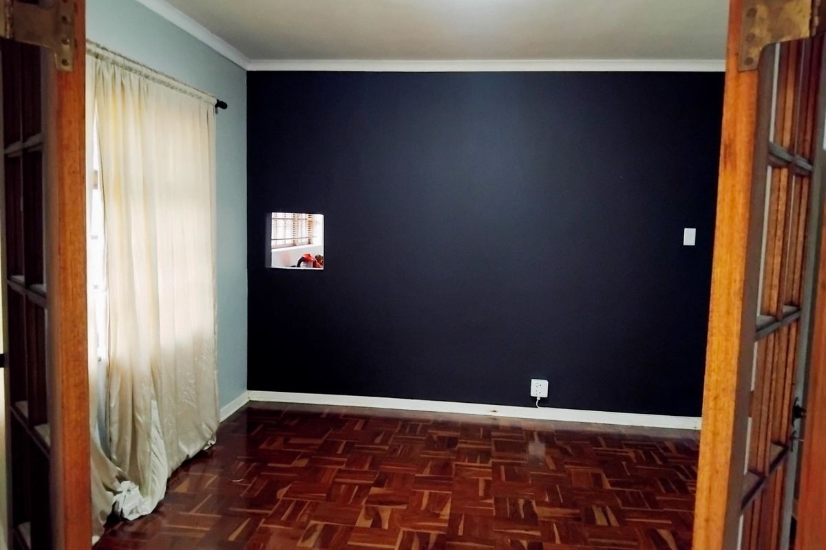 An empty bedroom featuring polished parquet flooring, a dark accent wall with a unique built-in cutout, and classic wooden door frames.
